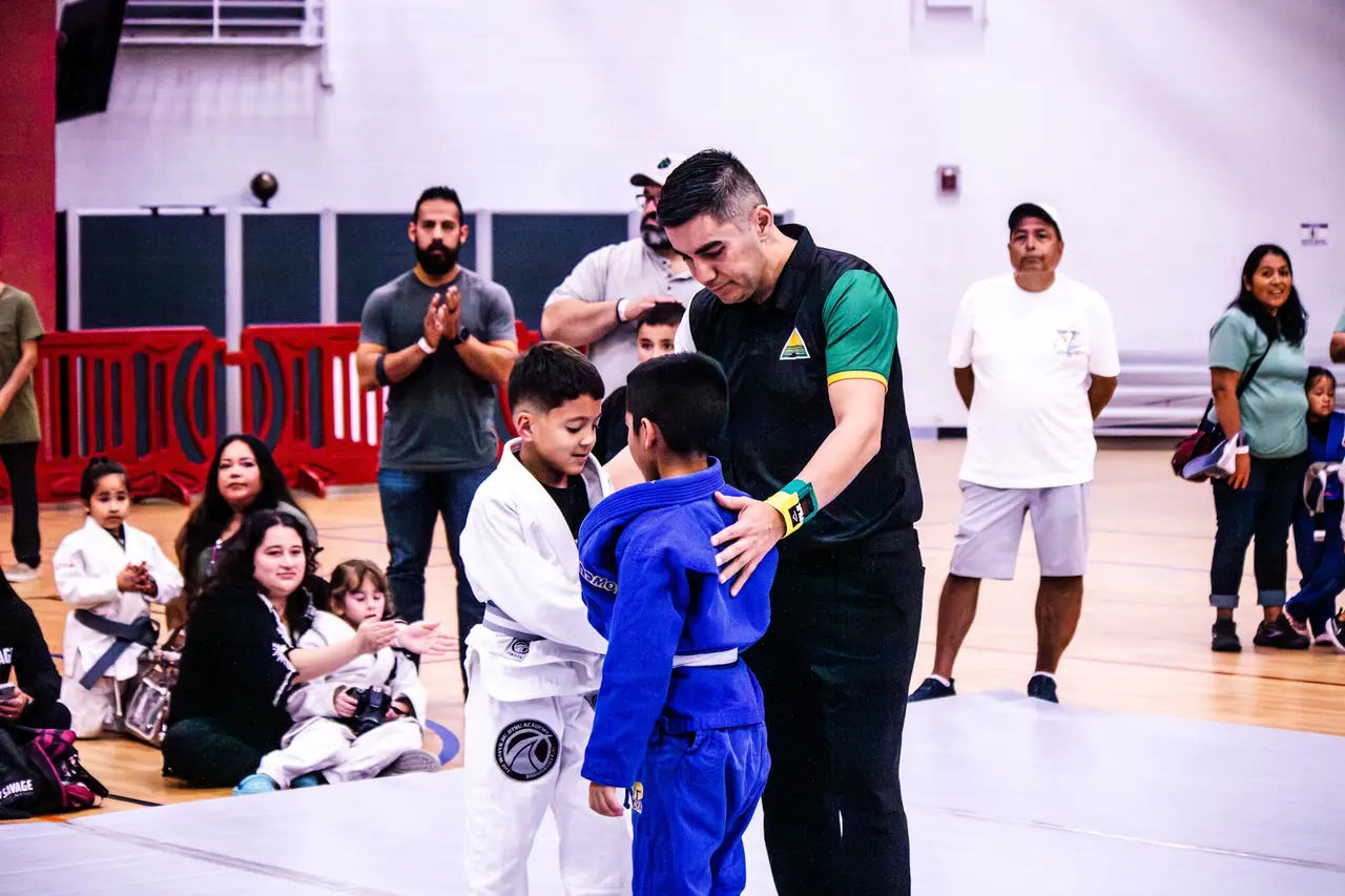 An RGV Open referee gets two young competitors in white and blue gis ready for their match.